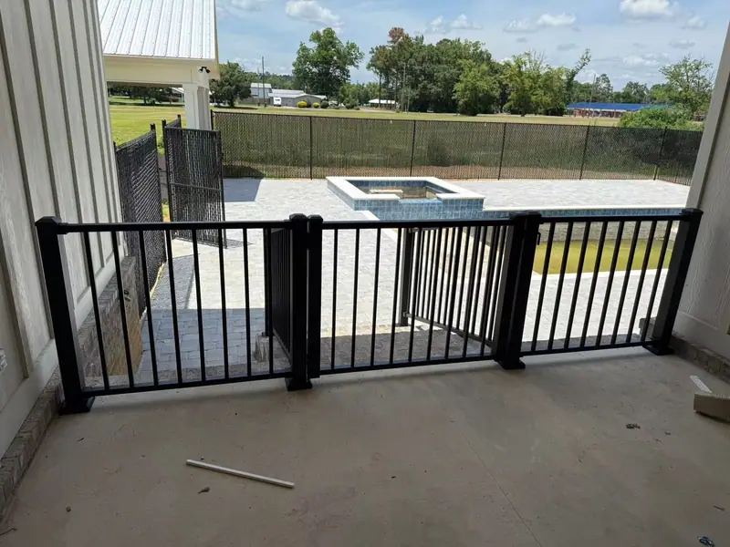 Black aluminum porch railing with a gate, looking out over a new pool deck enclosed by black chain link fence with privacy slats, a Southern Line Fence & Finish job