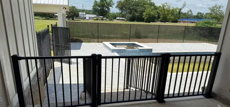Black aluminum railing and gate on a covered porch above a pool deck, with black chain link and privacy slats around the pool