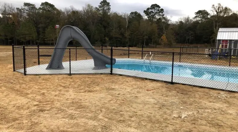 Black chain link pool fence around a new in-ground pool with a slide, built by Southern Line Fence & Finish