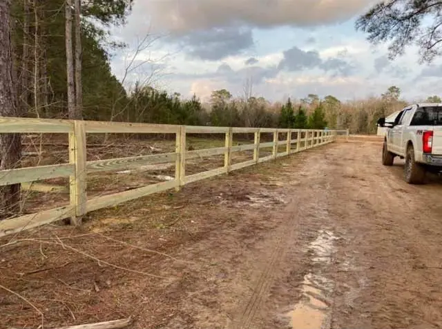 A new three-rail pine fence running along a red clay drive past a pickup truck, built by Southern Line Fence & Finish