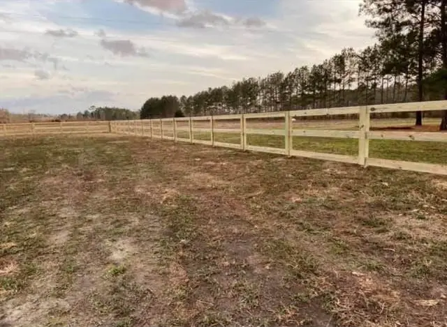 A three-rail pine fence stretching across an open pasture under a cloudy sky, a Southern Line Fence & Finish job