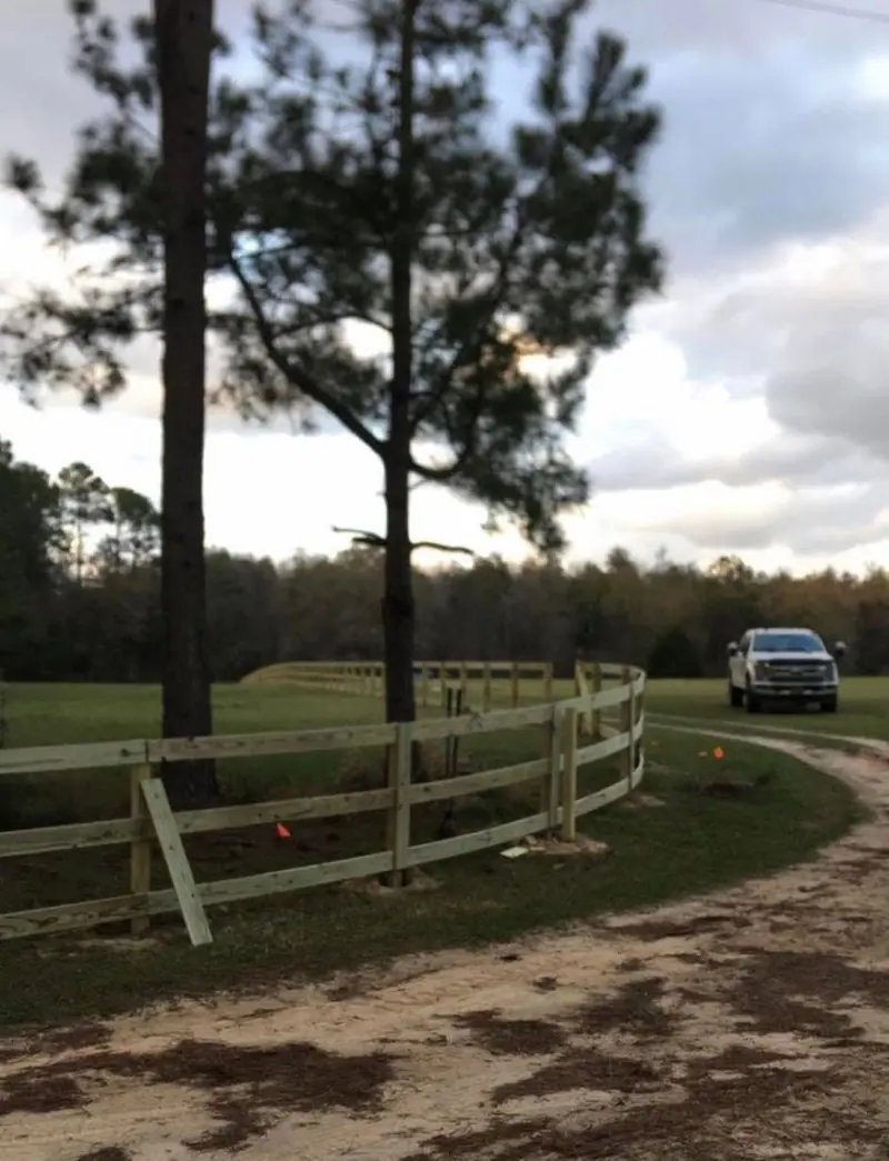 A three-rail fence curving with a sand drive under tall pines in Vernon, Florida, a Southern Line Fence & Finish job