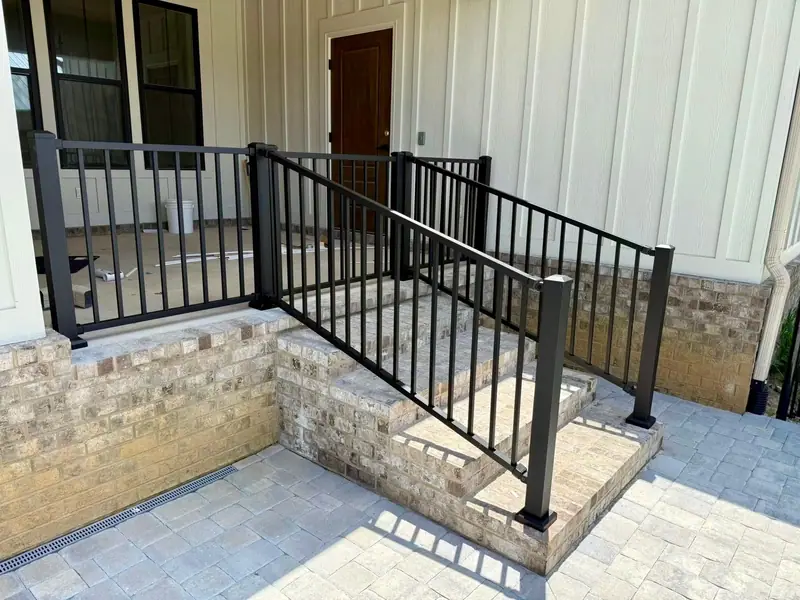 Black aluminum railing up the brick steps of a white board-and-batten porch, installed by Southern Line Fence & Finish