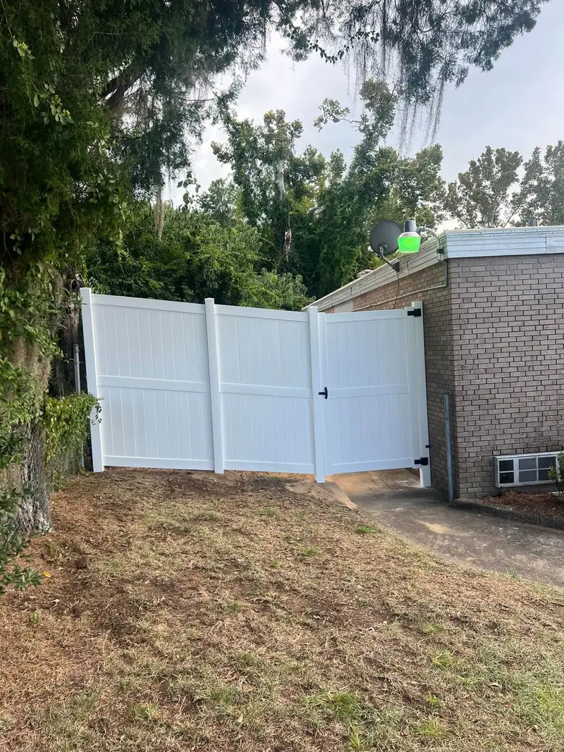 White vinyl privacy fence with a double gate beside a brick house, installed by Southern Line Fence & Finish