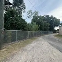 Galvanized chain link fence along a gravel alley under shade trees