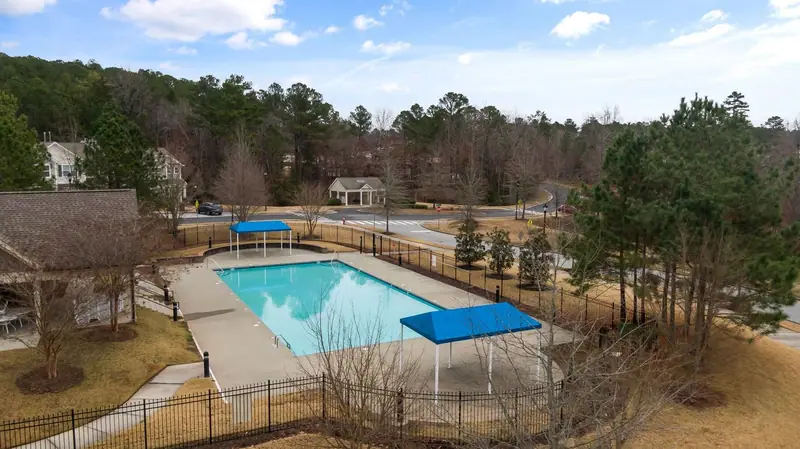 Aerial view of a community pool ringed by a black picket pool fence, with pines beyond