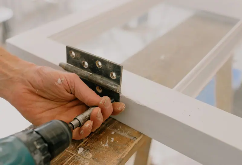 Hands screwing a steel hinge onto a gate frame with a cordless drill