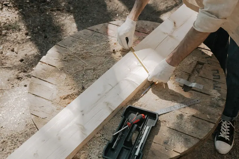 Gloved hands measuring a pine board with a tape